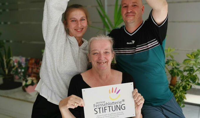 Sabine Bala und Patrick Bertelsbeck (hinten) sowie Ursula Kuchta (vorne) halten das Logo der Deutschen Fernsehlotterie Stiftung