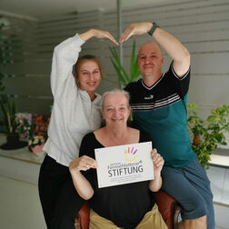 Sabine Bala und Patrick Bertelsbeck (hinten) sowie Ursula Kuchta (vorne) halten das Logo der Deutschen Fernsehlotterie Stiftung